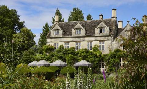 The stunning garden of The PIG - in the Cotswolds with umbrella shaded seating in front of the wisteria clad hotel