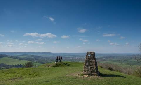 A group of people are standing looking out across rolling green fields under a blue sky with wispy clouds