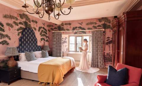 A bride stands by the window in a maximalist decorated bedroom at The Old Bell Hotel