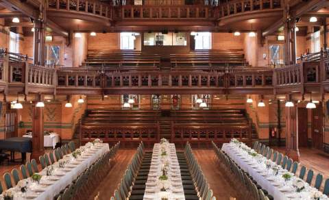 Long banqueting tables fill the length of a large wooden room with tiered balcony at Cheltenham Ladies College