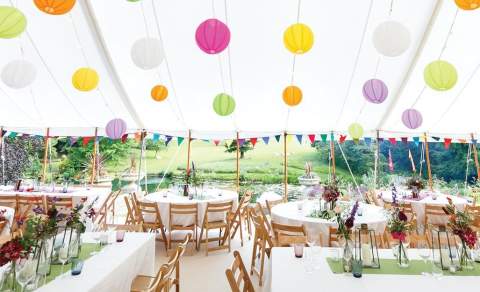 A marquee with brightly coloured ball lights hanging above tables decorated with fresh flowers at Cowley Manor
