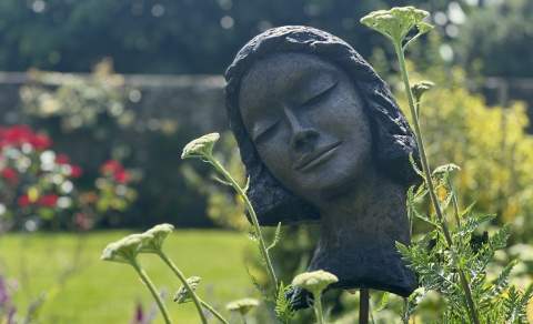 Sculpture of a head set amongst flowers and garden background