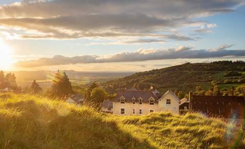Cleeve Hill Hotel nestled into the hillside as the sun sets behind trees in the distance
