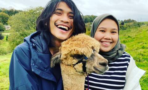 Two people smiling and posing with an alpaca