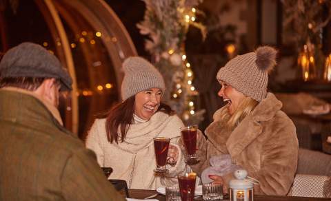 Two ladies in bobble hats enjoying mulled wine at a Christmas market at Wild Thyme and Honey