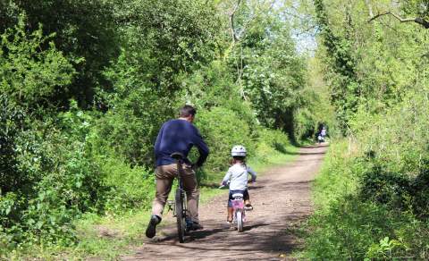 Father and daughter cycling down a leafy bridleway