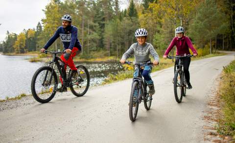Famile på sykkeltur på en grusvei langs et vann.