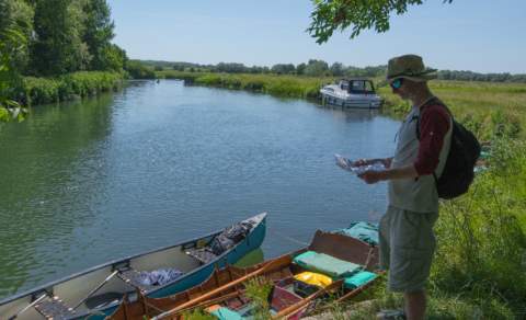 A man checks a map standing next to rowing boats moored on the River Thames, near Kelmscott