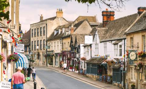 People walking and cycling along the High Street, which is decorated with flowering baskets and bunting, in Winchcombe in the Cotswolds