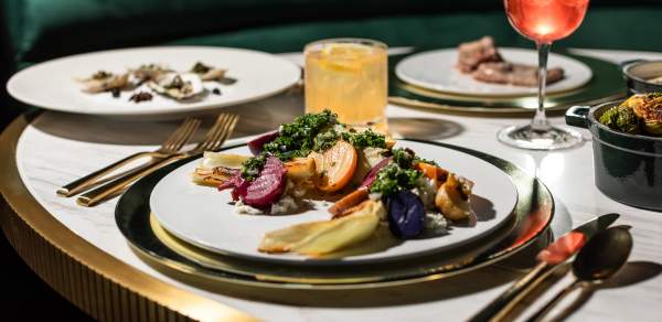 A table is set with multiple plates of brightly colored vegetables and a pink cocktail