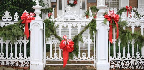 White cast iron fence with green leafy garland and red bows in front of a historic brick home