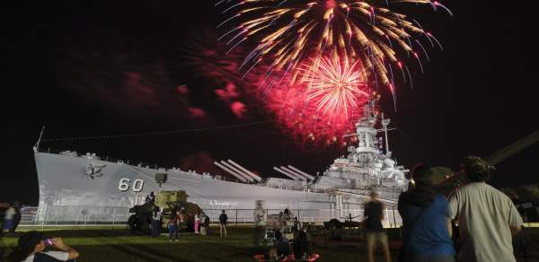 Red fireworks explode at night above the USS ALABAMA battleship