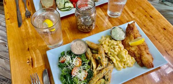 two plates of food on a table - fish, mac and cheese, fries, greens