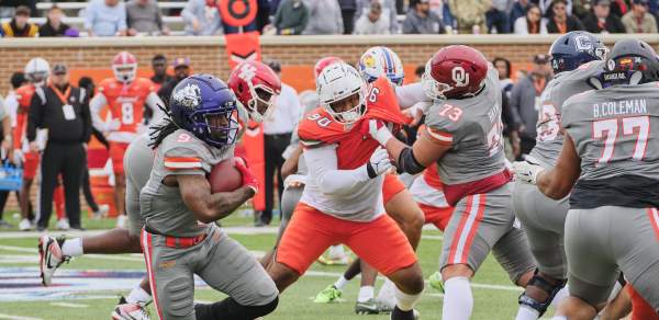 Football players in gray and orange jerseys, one player running with a football