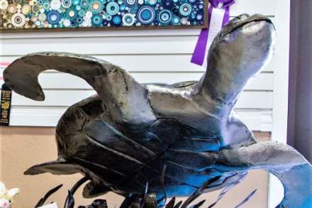 Art sculpture of a turtle with other art around it. Each has a fair ribbon on it