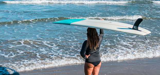 A woman holds a surfboard over her head as she watches the surf in Port Aransas, TX
