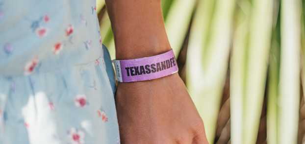 Close up on a woman's wrist that has a purple wristband on it reading "Texas SandFest"