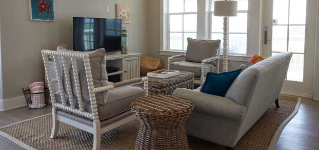 A living room with coastal decor in shades of beige. A tan couch faces a television and two chairs face each other perpendicular to the couch.