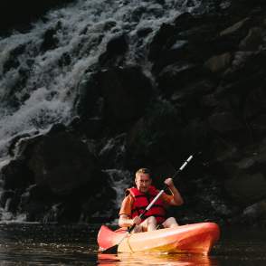 a man wearing a life-jacket and kayaking with a waterfall in the background