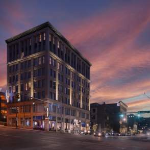 The illuminated Hotel BLU, a historic downtown building, stands on a city street corner beneath a vibrant pink and purple sunset sky.