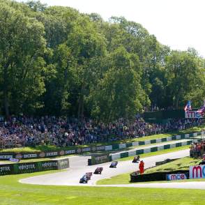A race track with motorbikes and audience stood around on grass banks