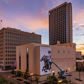 man working on mural of cowboy riding horse for Hoodoo Mural Festival on side of building in downtown amarillo
