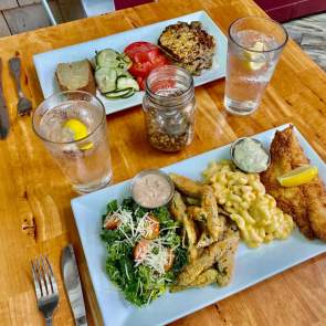 two plates of food on a table - fish, mac and cheese, fries, greens