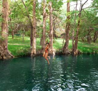 Image of a women jumping off a rope swing into Blue Hole in Wimberley, Texas.