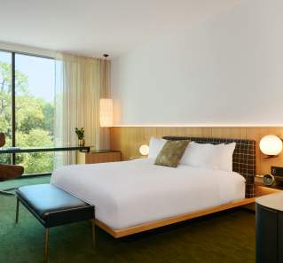 A hotel room with a bed, accent chair and large window at The Loren Hotel.