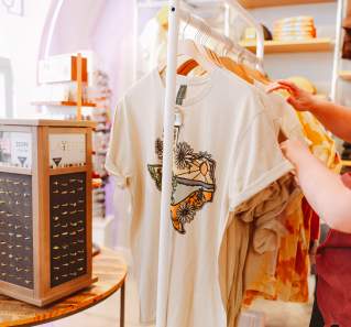 Arm reaching towards a t-shirt with an illustrated state of Texas on the front, on a clothing rack inside the Austin Visitor Center.