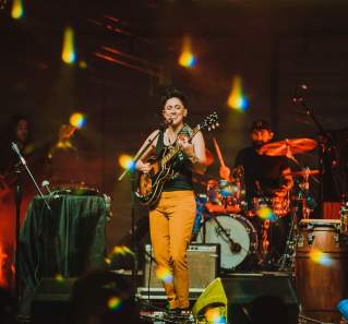 Gina Chavez on large stage with instruments in the background.