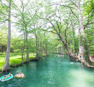 People floating on Blue Hole in pink and blue innertubes, with trees lining the shoreline.
