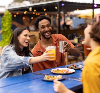 Two women and a man cheering drinks over plates of tacos.