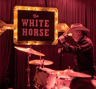 Man in a cowboy hat setting up a microphone on the stage at White Horse.