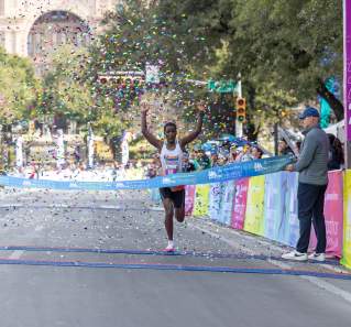 Image of a man crossing the finish line with his hands in the air at the Austin Marathon.