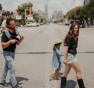 Family of four strolling across a crosswalk on South Congress Avenue with Texas State Capitol and Austin Motel in the background.