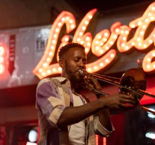 Austin musician Daniel Fears plays the trombone in front of The Liberty bar's lighted sign