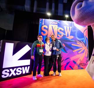 Conference attendees taking their picture in front of a SXSW mural in the registration area.