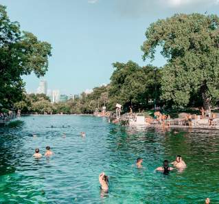 Adults and children playing in and along the banks of Barton Springs Pool.