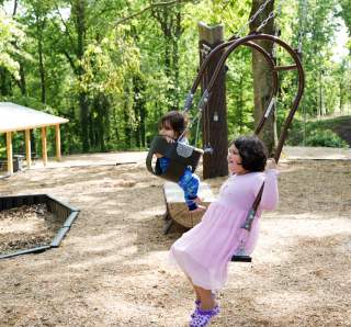 Two children swing on a double swing at Dunnavant Valley Park on a beautiful summer day.