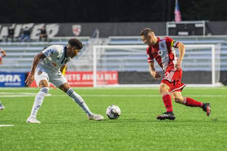 Loudoun United FC player in red dribbles past an opposing defender during a night match at Segra Field in Leesburg, Virginia