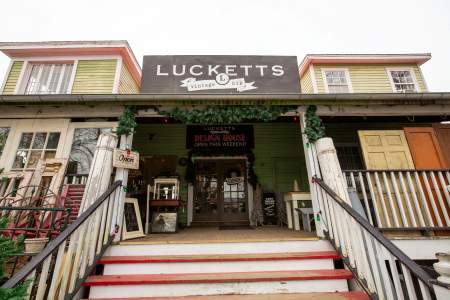 Exterior of Old Lucketts Antique Store with a green and red exterior. The entrance has festive greenery and various antiques displayed outside.