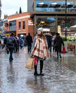 A woman in a scarf is stood in the centre of the Cornhill Quarter in Lincoln, holding shopping bags.