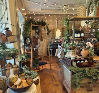 Picture of home good store with lights on ceiling, lots of greenery, platters, candles