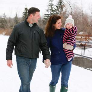 Couple with Baby Holding Hands and Walking through the Snow