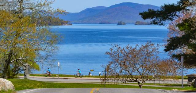 People biking along Beach Road with a view of Lake George
