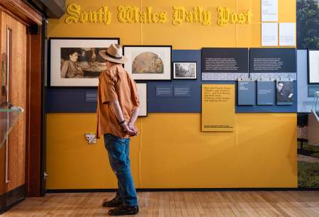 A man looking at picture in an exhibition on a yellow wall.