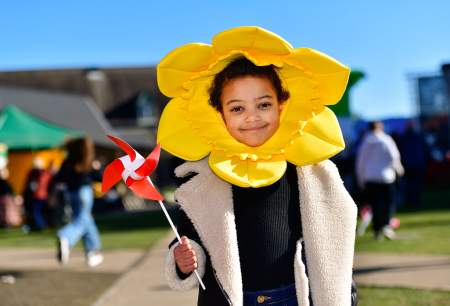 A child wearing a daffodil head dress, holding a windmill.