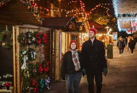 Young couple holding hands and exploring Swansea Christmas Market at night
