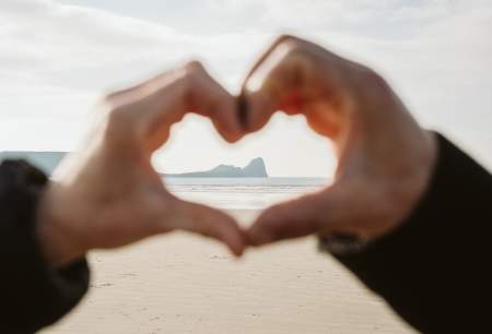 A close up of a pair of hands making a heart shape with Worm's head visible in the distance in the centre of the heart shape.